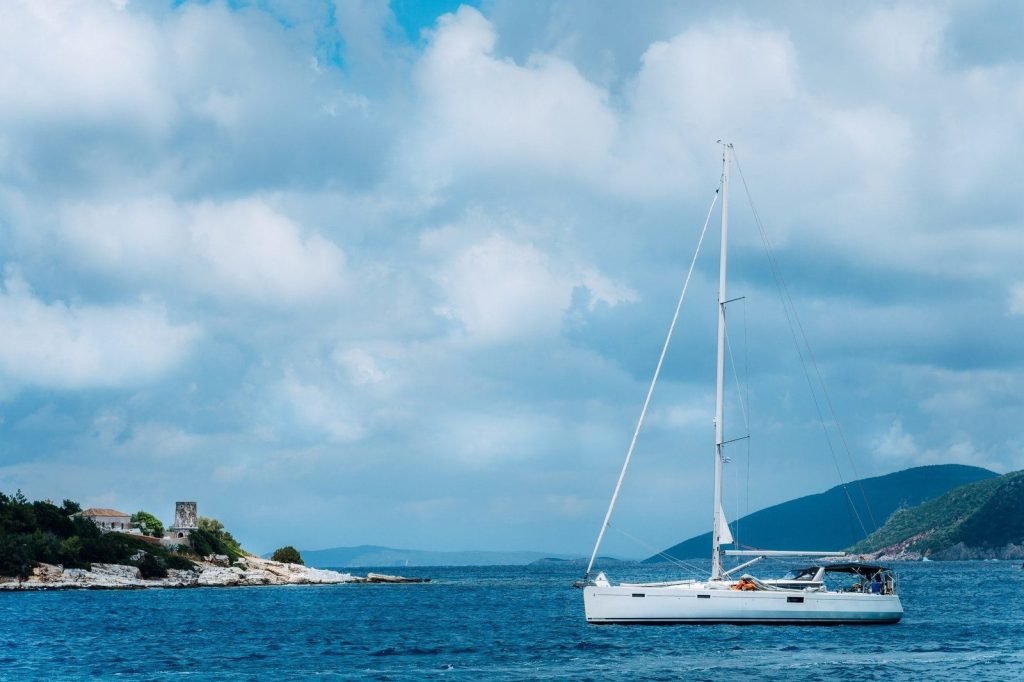 summer-scenery-of-port-fiskardo-white-sail-boat-in-beautiful-tranquil-bay-opposite-rocky-seashore